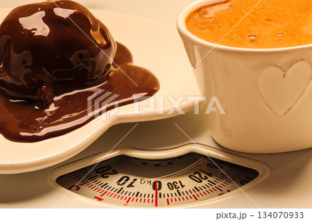 Coffee and chocolate cake on weighing scale. 134070933