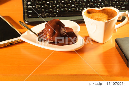 Cup of coffee and chocolate cake next to computer. Cup of coffee and chocolate cake next to computer. 134070934