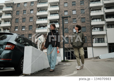 Two women walk outside with a border collie near modern apartment buildings. The scene illustrates companionship and the concept of active lifestyle 134070983