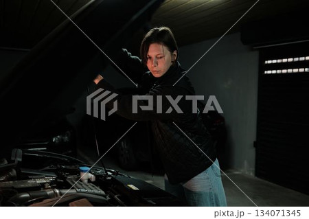 A woman opens the car hood and checks the engine compartment in an underground garage. The moment shows routine vehicle inspection and responsible car ownership A woman opens the car hood and checks the engine compartment in an underground garage. The moment shows routine vehicle inspection and responsible car ownership 134071345