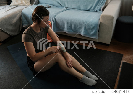 A woman uses a massage gun on her arm after training, focusing on muscle recovery and gentle relaxation in a peaceful home environment 134071418
