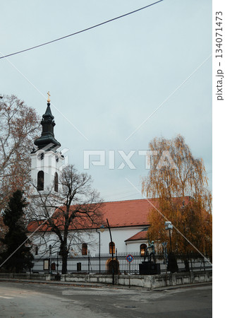 A white church with a dark spire rises above autumn trees in Sremski Karlovci, Serbia. The calm atmosphere highlights the historic and spiritual character of the town A white church with a dark spire rises above autumn trees in Sremski Karlovci, Serbia. The calm atmosphere highlights the historic and spiritual character of the town 134071473