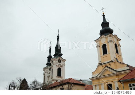 Twin baroque church towers in Sremski Karlovci, Serbia, rising over rooftops. A concept of religion, heritage, and cultural tourism Twin baroque church towers in Sremski Karlovci, Serbia, rising over rooftops. A concept of religion, heritage, and cultural tourism 134071499