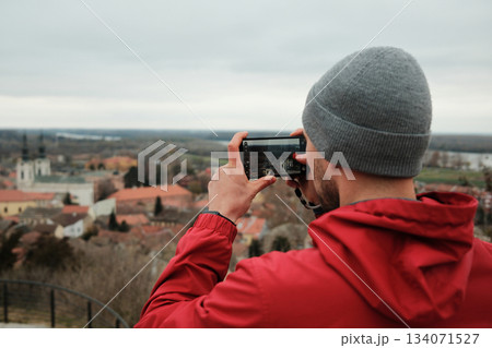 Traveler holds a smartphone and records the view of church towers and rooftops from a high point. The moment shows discovery and connection. Travel blogger concept Traveler holds a smartphone and records the view of church towers and rooftops from a high point. The moment shows discovery and connection. Travel blogger concept 134071527