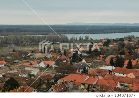 A wide view of Sremski Karlovci stretches toward the river and distant forest line. In the distance, a modern train can be seen racing along the Danube railway 134071677