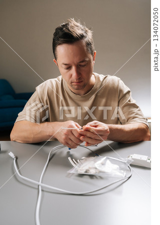 Vertical portrait of man working with electronic components, stripping insulation from cable repairing, assembling wiring, demonstrating hobby electronics project or household electrical maintenance. 134072050