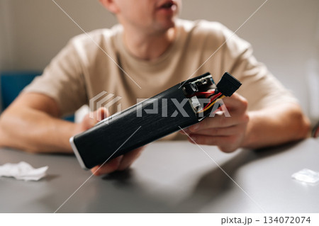 Cropped shot of technician working with electronic device, holding computer hardware with exposed cooling fan, performing repairs and maintenance on tech equipment in modern workshop environment. 134072074