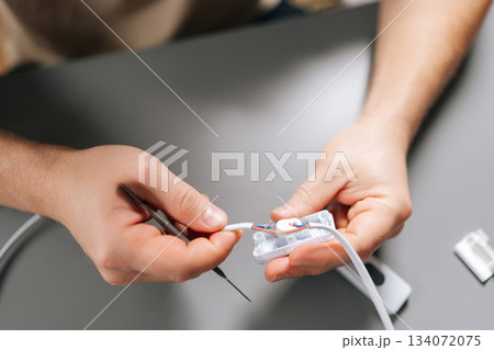 Close-up of male hands strip and reconnect damaged power cable inside white connector housing, showing precise wiring repair, tools and focused technical skill for restoration. 134072075