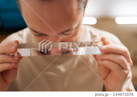 Man holding clear glass prism, looking over edge with eyes visible in prism reflection, interesting optical phenomenon and scientific exploration, curiosity, science, vision, and depth of field. 134072076