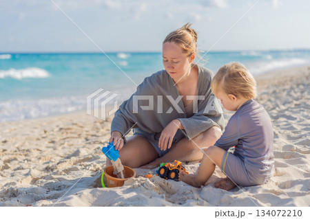 Woman spending quality time with her son on a sunny beach, enjoying the warmth, waves and playful bonding moments. Summertime leisure, family connection and coastal relaxation concept, representing 134072210