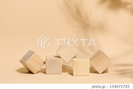 Five light wooden cubes placed in the center on a beige background with the soft shadow of a tropical palm leaf, create a clean, minimalist podium stage Five light wooden cubes placed in the center on a beige background with the soft shadow of a tropical palm leaf, create a clean, minimalist podium stage 134072785
