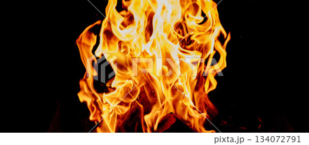 Close-up of tall bright flames, tongues of fire and orange-yellow glow above burning logs Close-up of tall bright flames, tongues of fire and orange-yellow glow above burning logs 134072791