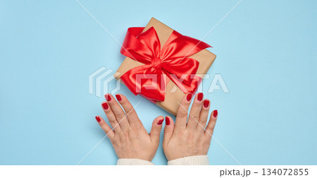 A gift box wrapped in a red satin ribbon and two female hands, the process of gift giving and congratulations 134072855