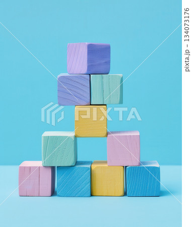 Pastel Wooden Blocks Stacked in Tower on Blue Background, minimal composition of pastel-colored wooden blocks arranged in pyramid shape against clean blue background Pastel Wooden Blocks Stacked in Tower on Blue Background, minimal composition of pastel-colored wooden blocks arranged in pyramid shape against clean blue background 134073176