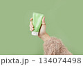 A womans hand in a sweater holds a tube of cream on a green background. Self care beauty treatment 134074498