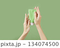 A womans hands holding a tube of lotion on a green background. Body care 134074500