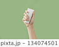 A womans hand holding a white cosmetic tube on a green background 134074501