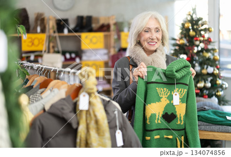 Elderly woman chooses fashionable sweater for winter season in store 134074856