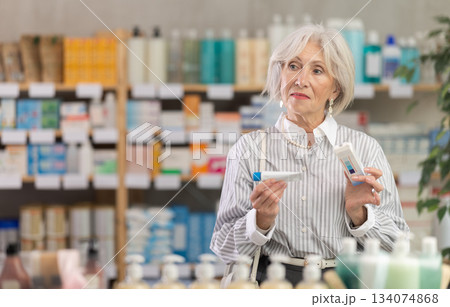 Elderly woman chooses ointment at pharmacy 134074868