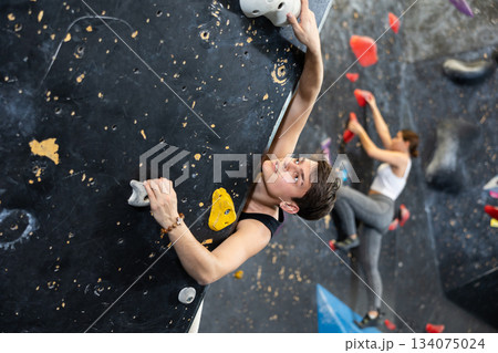 Sporty strong young man exercising in boulder climbing hall without rope, reaching new results, enjoying new challenges in amusement park Sporty strong young man exercising in boulder climbing hall without rope, reaching new results, enjoying new challenges in amusement park 134075024