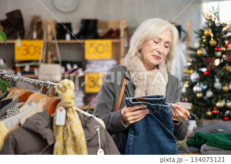 Glad mature woman choosing jeans pantaloons in clothing store Glad mature woman choosing jeans pantaloons in clothing store 134075121