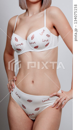 Woman in a white floral lace lingerie set posing with one foot slightly raised Woman in a white floral lace lingerie set posing with one foot slightly raised 134075158