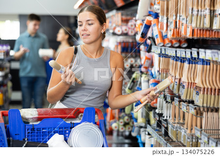 Positive female shopper buying paint brushes at hardware store 134075226