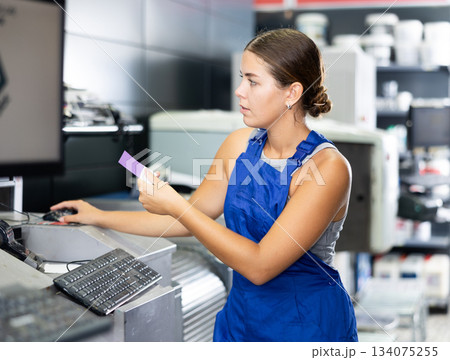 Hardware store employee combining just the right tints of paint in an electronically guided modern mixing machine Hardware store employee combining just the right tints of paint in an electronically guided modern mixing machine 134075255