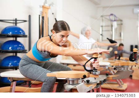Young girl during Pilates training performs exercises and tasks on heron pulley tower Young girl during Pilates training performs exercises and tasks on heron pulley tower 134075303