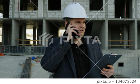 Construction talking on a smartphone while overlooking the busy work site 134075324