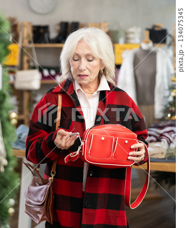 Uncertain mature woman choosing handbag in clothing store 134075345