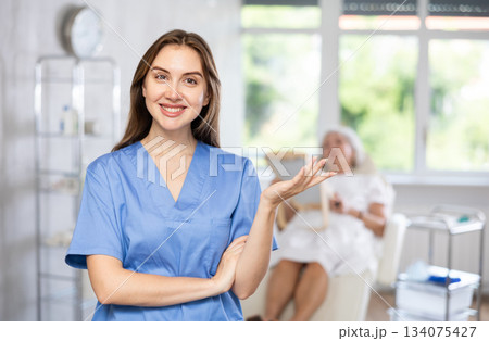 Female doctor cosmetologist stand with woman looking mirror behind in the doctors office. Female doctor cosmetologist stand with woman looking mirror behind in the doctors office. 134075427