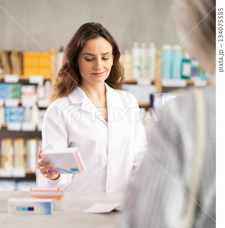 female pharmacist advises a client behind the counter in a pharmacy 134075585