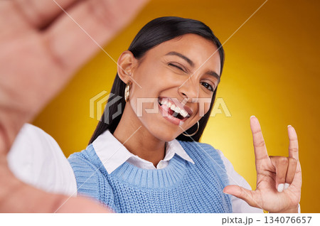 Selfie, rock sign and portrait of Indian woman in studio for happiness, confident and wink on yellow background. Mockup, fashion and girl with punk hand gesture with beauty, cosmetics and makeup 134076657