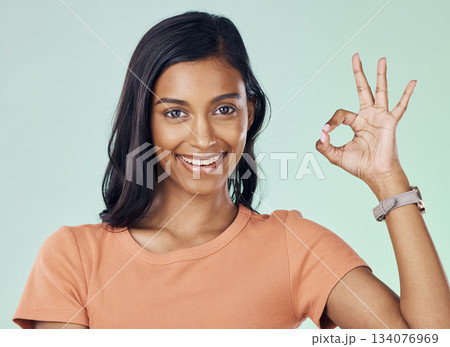 Portrait, perfect hand gesture and woman in a studio with a positive, confident and happy mindset. Happiness, smile and young Indian female model with a ok sign language isolated by green background. Portrait, perfect hand gesture and woman in a studio with a positive, confident and happy mindset. Happiness, smile and young Indian female model with a ok sign language isolated by green background. 134076969