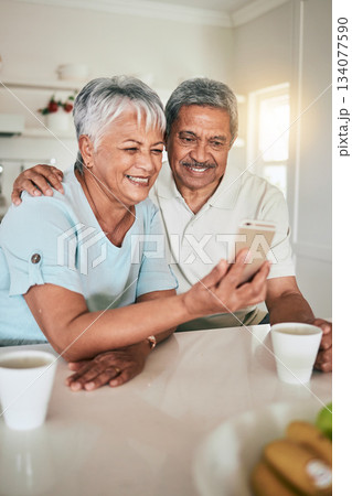 Phone, video call and elderly couple in a kitchen happy, smile and embrace in their home. Smartphone, love and old people pose for selfie, photo or profile picture while enjoying retirement together 134077590