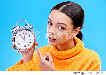 Woman, annoyed and point at alarm clock in portrait for warning by blue background in studio. Gen z girl, student and model with watch, time management and schedule with angry face to start morning 134078584
