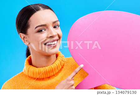 Speech bubble, smile and portrait of woman pointing to banner in studio for advertising on blue background. Face, happy and girl with poster, mockup and space for social media, announcement or news 134079130