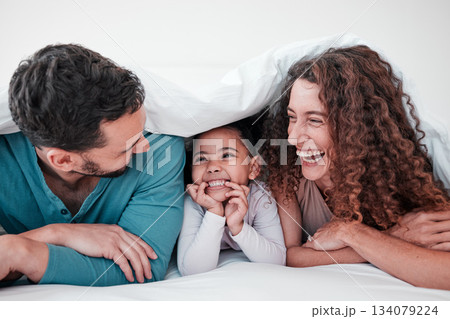Family in bed, parents laughing with child and relax with smile under blanket in bedroom with love and care. Spending time together, bonding and relationship, man and woman with young girl at home 134079224