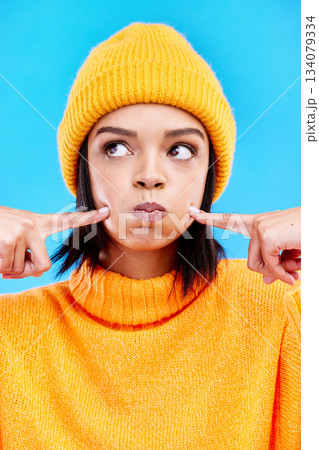 Silly, goofy and young woman in a studio with a comic, funny and crazy face expression. Funny, humor and beautiful female model from Puerto Rico touching her cheeks isolated by a blue background. 134079334