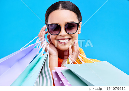 Shopping bags, studio and happy woman portrait with a smile and happiness from boutique sale. Sunglasses, customer and female model with store bag and sales choice in isolated blue background Shopping bags, studio and happy woman portrait with a smile and happiness from boutique sale. Sunglasses, customer and female model with store bag and sales choice in isolated blue background 134079412