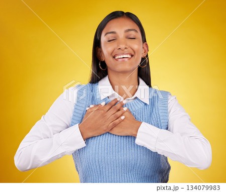 Gratitude, happy and young woman in a studio with her hand on her chest for a grateful expression. Happiness, smile and Indian female model with a thankful hand gesture isolated by yellow background. Gratitude, happy and young woman in a studio with her hand on her chest for a grateful expression. Happiness, smile and Indian female model with a thankful hand gesture isolated by yellow background. 134079983