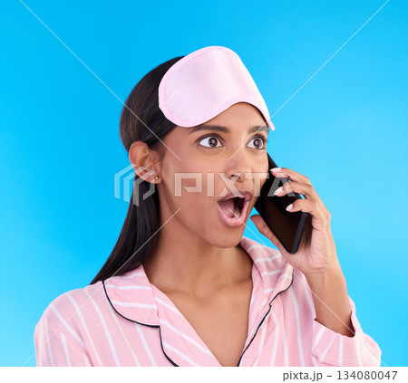 Phone call, shock and woman in pajamas in a studio with shocking, winning or good news. Surprise, happy and Indian female model on a mobile conversation with a wtf, omg or wow face by blue background 134080047