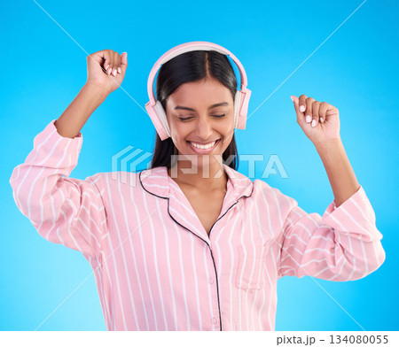 Happy, dance and woman in pajamas, headphones and cheerful on a blue studio background. Female, joyful and lady with headset, waking up and dancing with sounds, streaming music and songs for movement 134080055
