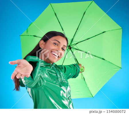 Portrait, smile and woman with umbrella, excited and expression against blue studio background. Face, female and person with cover from rain, happiness and excitement with joy, adventure or insurance 134080072