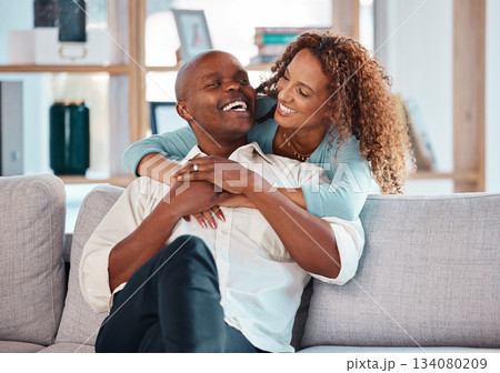 Couple, hug and laughing on sofa in home living room, bonding, relaxing and having fun. Interracial, love and funny black man and woman on couch embrace, happiness and enjoying quality time together 134080209