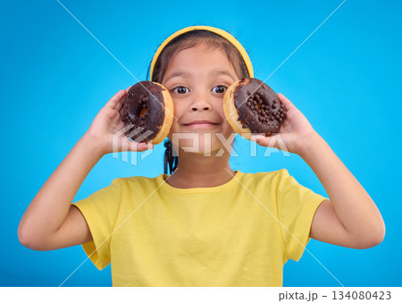 Donut, happy and smile with portrait of girl in studio for junk food, sugar and happiness. Snack, cake and cute with face of child and dessert for eating, diet and chocolate on blue background Donut, happy and smile with portrait of girl in studio for junk food, sugar and happiness. Snack, cake and cute with face of child and dessert for eating, diet and chocolate on blue background 134080423