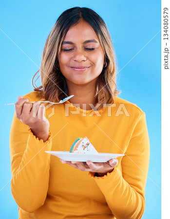 Woman, fork and cake in studio for dessert, satisfied or eyes closed for happiness by blue background. Indian model, girl and happy for eating sweets, snack and test flavor for food, meal and diet 134080579