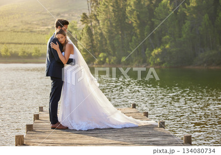 Wedding couple, hug and love by lake in nature for relax or romantic honeymoon getaway. Calm woman hugging man in happy marriage relaxing by water together enjoying the loving embrace outdoors 134080734