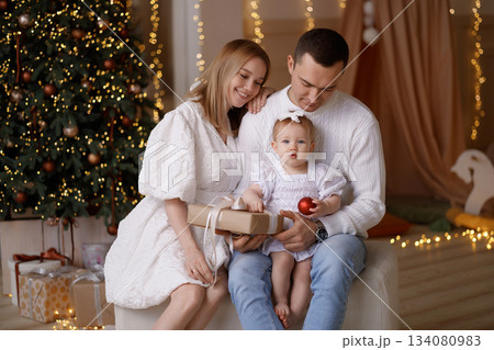 Happy young family with baby girl celebrating Christmas at home near decorated tree Happy young family with baby girl celebrating Christmas at home near decorated tree 134080983